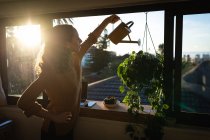 Кавказька жінка проводить вдома самоізоляцію і соціальну дистанцію в карантині під час ішемічної хвороби коронавірусу 19, поливаючи рослини на кухні.. — стокове фото
