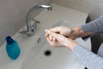 Feche no meio da seção da mulher usando camisola cinza, lavando as mãos com sabão líquido. Distanciamento social e auto-isolamento em quarentena . — Fotografia de Stock