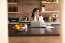 Женщины смешанного расового происхождения проводят время дома, работая из дома с помощью ноутбука на кухне. Самоизоляция и социальное дистанцирование в карантинной изоляции во время эпидемии коронавируса ковида 19. — стоковое фото