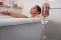 Змішана жінка проводить час вдома, лежачи у ванній, розслабляючись з закритими очима у ванній кімнаті. Самоізоляція та соціальне дистанціювання в карантинному блокуванні під час епідемії коронавірусу 19 . — стокове фото