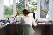 Rear view of mixed race woman spending time at home self isolating and social distancing in quarantine lockdown during coronavirus covid 19 epidemic, sitting at desk using computers working from home — Stock Photo