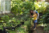 Una donna caucasica e sua figlia si divertono insieme in un giardino soleggiato, usando un tubo da giardino per innaffiare le piante. — Foto stock