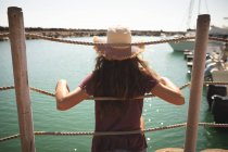 Підліток кавказка, одягнена в солом'яний капелюх, насолоджуючись своїм часом на променаді, в сонячний день, сидячи і спираючись на бар'єр, озираючись на — стокове фото