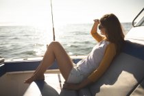 Une adolescente caucasienne profite de ses vacances au soleil au bord de la côte, assise sur un bateau, relaxante, regardant ailleurs — Photo de stock