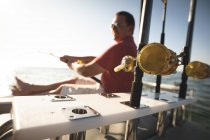 A Caucasian man enjoying his time on holiday in the sun by the coast, sitting on a boat, holding a fishing rod — Stock Photo