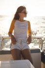 Una adolescente caucásica disfrutando de su tiempo de vacaciones en el sol junto a la costa, de pie en un barco, inclinada, relajada, mirando hacia otro lado - foto de stock