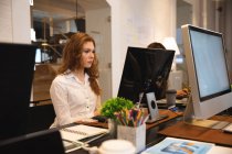 Negocio femenino caucásico creativo que trabaja en una oficina moderna informal, sentado en un escritorio y usando una computadora con un colega que trabaja junto a ella - foto de stock