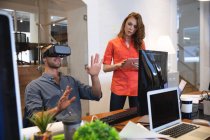 Femmes et hommes d'affaires créatifs caucasiens travaillant dans un bureau moderne décontracté, un homme utilisant un casque VR et une femme utilisant une tablette — Photo de stock