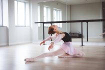 Кавказская привлекательная балетная танцовщица с рыжими волосами, готовящаяся к балетному классу в яркой студии, сосредоточенная на упражнениях, сидящая на полу. — стоковое фото