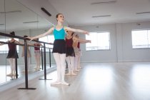 Un groupe de danseuses caucasiennes attirantes s'étirant, tenant une barre dans un studio de ballet lumineux, se concentrant sur leur exercice, se préparant pour un cours de ballet. — Photo de stock