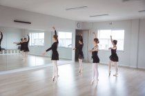 Un grupo de bailarinas de ballet caucásicas atractivas con trajes negros practicando durante una clase de ballet en un estudio brillante, bailando frente a un espejo. - foto de stock