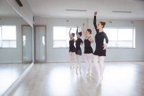 Un groupe de danseuses caucasiennes séduisantes en costumes noirs pratiquant pendant un cours de ballet dans un studio lumineux, dansant devant un miroir. — Photo de stock