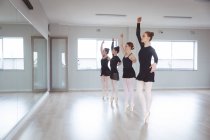 Eine Gruppe attraktiver kaukasischer Balletttänzerinnen in schwarzen Anzügen übt während eines Ballettkurses in einem hellen Studio vor einem Spiegel. — Stockfoto