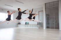 Група кавказьких танцюристок привабливого балету в чорному одязі, що практикується під час класу балету в яскравій студії, танцюють і стрибають в повітря в унісон.. — стокове фото