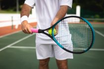 Средняя часть мужчины в теннисных белках проводит время на корте, играя в теннис в солнечный день, держа теннисную ракетку и мяч — стоковое фото