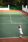 Un caucasico e un uomo di razza mista che indossano i bianchi del tennis trascorrono del tempo insieme su un campo, giocando a tennis in una giornata di sole, uno di loro si prepara a colpire una palla — Foto stock