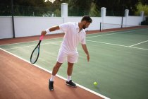 Un uomo di razza mista che indossa i bianchi del tennis trascorre del tempo su un campo a giocare a tennis in una giornata di sole, preparandosi a colpire una palla — Foto stock