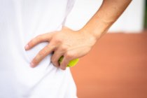 Gros plan d'une main d'homme portant des blancs de tennis passant du temps sur un court jouant au tennis par une journée ensoleillée, tenant une balle de tennis — Photo de stock