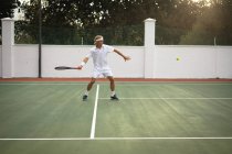 Un homme caucasien portant des blancs de tennis passe du temps sur un court de tennis par une journée ensoleillée, tenant une raquette de tennis, se préparant à frapper une balle — Photo de stock