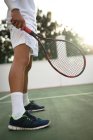 Средняя часть мужчины в теннисных белках проводит время на корте, играя в теннис в солнечный день, держа теннисную ракетку — стоковое фото
