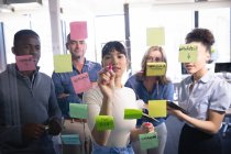 Um grupo diversificado de empresários que trabalham em um escritório moderno, brainstorming escrever em placa clara com notas de memorando, visto através — Fotografia de Stock