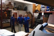 Троє з кавказьких і афроамериканських чоловіків на складі на заводі роблять інвалідні візки, стоять і розмовляють, двоє з них інваліди і використовують милиці. — стокове фото