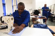 Ein afroamerikanischer Arbeiter in einer Werkstatt in einer Fabrik, die Rollstühle herstellt, sitzt an einer Werkbank und bedient eine Nähmaschine — Stockfoto