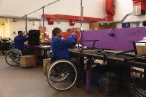 Dois trabalhadores afro-americanos deficientes em uma oficina em uma fábrica de cadeiras de rodas, sentados em uma bancada de trabalho montando partes de um produto, sentados em cadeiras de rodas — Fotografia de Stock