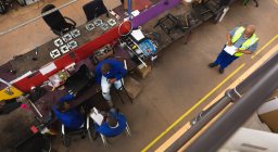 Группа афроамериканских рабочих-мужчин-инвалидов в мастерской на фабрике по производству инвалидных колясок, сидящих на рабочем столе, собирающих части продукта, двое сидят в инвалидных колясках, один с костылями — стоковое фото