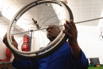 Афроамериканський робітник на фабриці виготовляє інвалідні візки, стоїть і перевіряє колесо, вдягнений у робочий одяг. — стокове фото