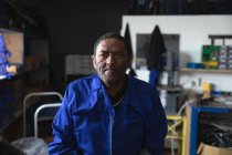 Портрет афроамериканца, одетого в рабочую одежду, на складе на фабрике, делающего инвалидные коляски, смотрящего в камеру — стоковое фото