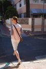 Uma mulher de negócios caucasiana em movimento em um dia ensolarado, andando em uma rua da cidade e segurando um café takeaway, usando óculos escuros — Fotografia de Stock