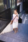 Une femme d'affaires caucasienne en déplacement par une journée ensoleillée, marchant dans les escaliers, parlant sur son smartphone et portant une smartwatch — Photo de stock
