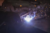 Gros plan d'un ouvrier d'usine portant des gants de sécurité, debout sur un établi, soudant. Travailleurs de l'industrie dans une usine de fabrication d'équipements hydrauliques. — Photo de stock