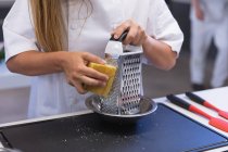 Mid section view of female chef grating hard cheese on a grater. — Stock Photo