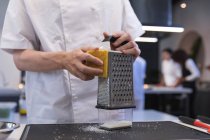 Vista de mitad de la sección de chef hembra rallando queso duro en un rallador. - foto de stock