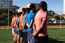 Мульти-этническая группа мужчин пять футболистов на стороне футболистов в спортивной одежде тренировки на спортивной площадке на солнце, стоя в ряд перед игрой. — стоковое фото