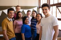 Frontansicht einer multiethnischen Gruppe von Teenagern, die zusammen in einem Klassenzimmer stehen und in der Pause in die Kamera lächeln — Stockfoto