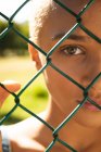 Close up portrait of mixed race alternative woman with short blonde hair out and about in the city on a sunny day, looking through a chain link fence. Urban independent woman on the go. — Stock Photo