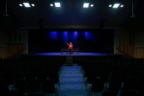 Vista frontal de uma adolescente de raça mista em pé no palco segurando um roteiro em um teatro escolar vazio durante os ensaios para uma performance — Fotografia de Stock