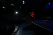 Seitenansicht eines Teenagers mit gemischter Rasse, der während der Proben für eine Aufführung in einem leeren Schultheater auf der Bühne steht und ein Drehbuch hält — Stockfoto