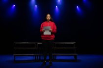 Вид спереду змішаної раси дівчина-підліток, що стоїть на сцені, тримає сценарій у порожньому шкільному театрі під час репетицій для виступу — стокове фото