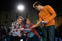 Front view of two Caucasian teenage boys and a mixed race teenage girl in discussion, holding scripts and smiling in the auditorium of an empty school theatre during rehearsals for a performance — Stock Photo