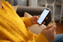 Seitenansicht Mitte einer Frau, die es sich zu Hause gemütlich macht, auf einem Sofa sitzt, eine Kreditkarte in der Hand hält und mit ihrem Smartphone einen Online-Kauf tätigt — Stockfoto
