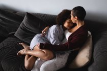 Vue grand angle du couple mixte féminin se détendre à la maison dans le salon, assis sur le canapé ensemble embrassant le matin — Photo de stock