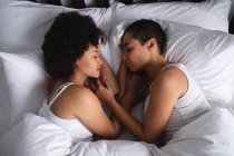 High angle close up view of a mixed race female couple at home in the bedroom, lying asleep in bed together in the morning, facing each other — Stock Photo