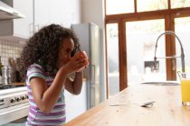 Seitenansicht eines jungen afroamerikanischen Mädchens zu Hause in der Küche, das auf der Kücheninsel steht und Frühstücksflocken aus der Schüssel isst — Stockfoto