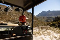 Visão traseira do homem caucasiano desfrutando do tempo na natureza, em equipamento de tirolesa sentado em um carro em um dia ensolarado nas montanhas — Fotografia de Stock