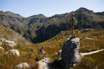 Vue latérale du couple caucasien profitant du temps dans la nature ensemble, portant un équipement de tyrolienne, randonnée, l'homme debout sur un rocher par une journée ensoleillée dans les montagnes — Photo de stock