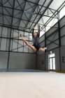 Низький кут зору на підлітків змішаної раси гімнастка виступає в спортзалі, стрибає і робить розкол, стрибає і робить розкол, носить чорно-фіолетовий леопард — стокове фото